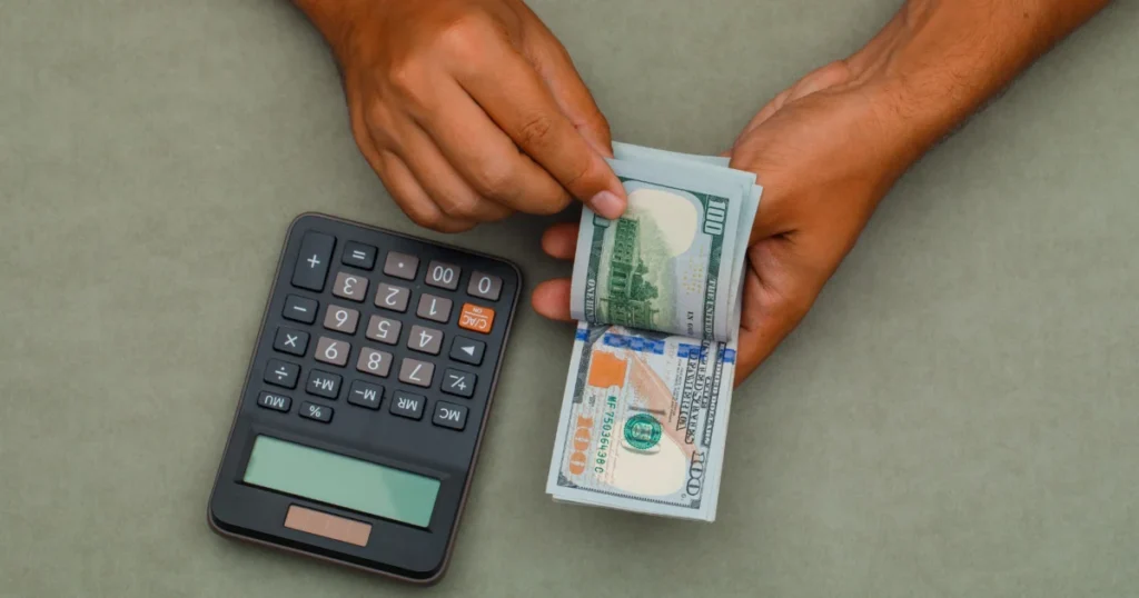 Hands counting US dollar notes beside a calculator to work out a USD loan repayment